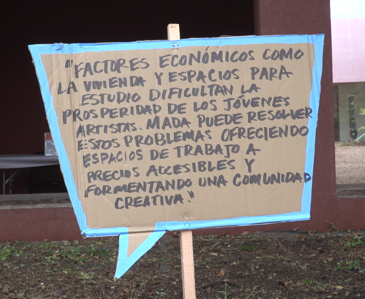 A hand-written sign reading -- Economic factors such as housing and spaces for study hinder the prosperity of young artists. MADA can address these problems by offering affordable workspaces and fostering a creative community.